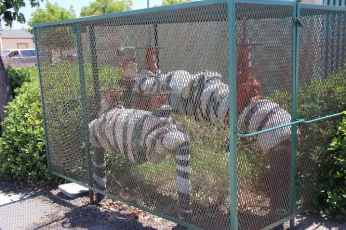 Large piping that is running into the ground and is surrounded by a chain link fence.