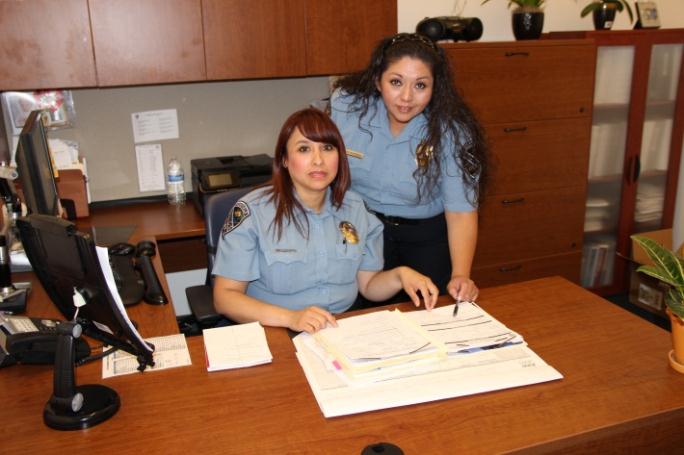 Two police officers sitting at a wooden desk.