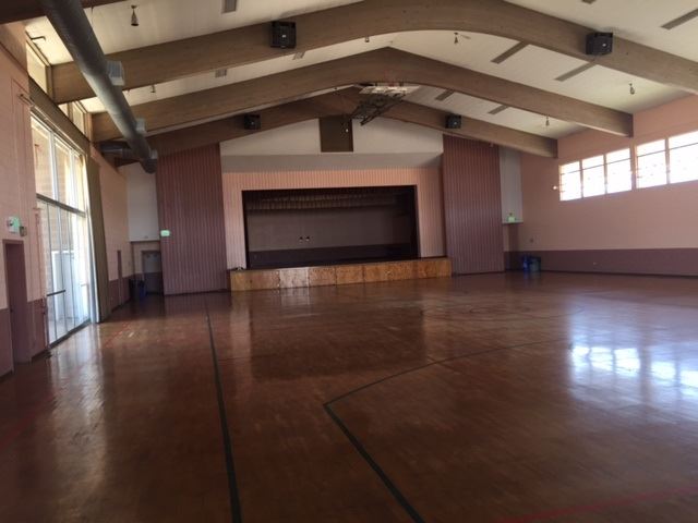 The inside of Memorial Hall. A large room with a basketball court floor and a stage at the end.