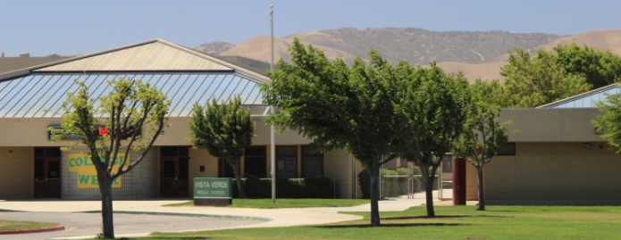 A metal school building with a row of trees in front of it.